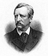 Head and shoulders portrait of a middle-aged man, facing half-left. He has dark, neatly brushed hair, a heavy moustache, and is wearing a dark, formal jacket.