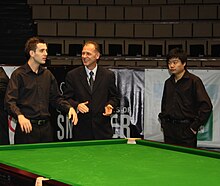 Three men by a snooker table, with Mark Selby on the left and Ding on the right.