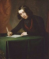 A man with shoulder-length black hair, sitting at a desk, writing with a quill