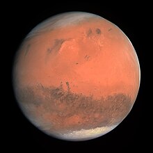 Mars appears as a red-orange globe with darker blotches and white icecaps visible on both of its poles.