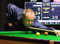 Photograph of John Higgins with a cue in hand, ready to strike the cue ball.