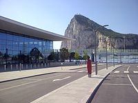 View of a modern glass—fronted building with a roadway in the foreground and the Rock of Gibraltar visible in the background