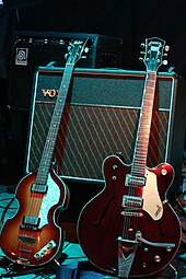Two electric guitars, a light brown violin-shaped bass and a darker brown guitar resting against a Vox amplifier