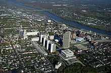 An aerial view of Albany showing tall buildings at center, a river running from the 11:00 to 3:00 positions of the photo, surrounded by greener housing zones.