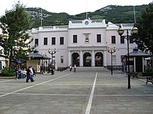 A long plaza with a large two—storey pink building at the far end, with a flight of steps leading up to the building's triple—arched entrance framed with columns.
