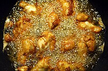 Chicken wings being fried in a pan filled with corn oil