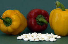 Two yellow and one red pepper with dozens of 500 mg white vitamin tablets in front of them