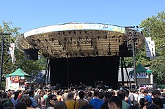 The covered stage known as Summerstage with a band entertaining a crowd of people