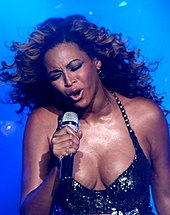 The upper body of a woman is shown as she sings into a microphone