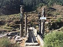 A wooden bridge in Sinja Valley with wooden pillars on either side, their top sculpted to depict human figures standing on the platform.