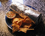 A Mission-style burrito, wrapped in aluminum foil, with tortilla chips and salsa
