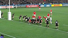The All Blacks lined up along their try-line, with a ruck formed several metres (yards) from the try-line. Several Tongan players are positions in or around the ruck waiting for the ball to emerge.