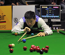 Ding leaning over a snooker table and lining up a shot