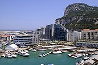 Yachts and boats anchored in a marina that lined with jetties and modern apartment blocks, with the Rock of Gibraltar in the background