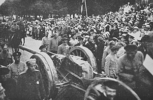 Foto de una escena durante la Guerra de Independencia de Letonia en el norte de Letonia, con una batería de artillería paseando y una bandera ondeando desde atrás.