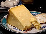 A wedge of yellow-white cheese, with a large crumbly piece broken off, served with a cracker