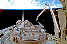 A Space Shuttle in space, with Earth in the background. A mechanical arm labelled "Canada" rises from the Shuttle.