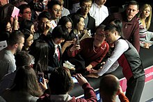 Ding poses for a photograph with a fan. Many other fans are nearby.
