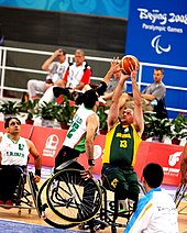 an athlete tilts his wheelchair and raises an arm to block his opponent's shot