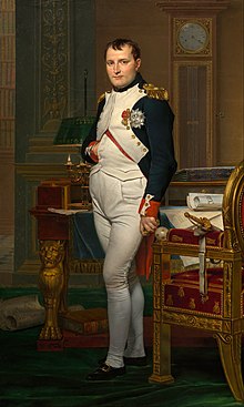 Retrato de Napoleón en sus treintas, con uniforme militar blanco y azul oscuro de alto rango.  En la imagen original, se encuentra en medio de ricos muebles del siglo XVIII cargados de papeles y mira al espectador.  Su cabello es estilo Brutus, muy corto pero con un flequillo corto al frente, y su mano derecha está metida en su chaleco.
