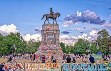 A bronze statue of a man riding a horse on a tall pedestal that is covered in colorful graffiti.