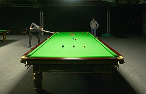 Ein Spieler, der an einem Übungs-Snooker-Tisch schießt und vom anderen Ende des Tisches aus mit einem niedrigen Kamerawinkel fotografiert wird, um eine erzwungene Perspektive zu erhalten