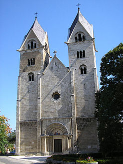 The facade of a tall grey church with paired towers and a single ornately carved doorway