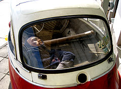 Tiny red and white bubble car, viewed from the rear, with a dummy in the rear representing a person being concealed in the car.