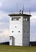 A squat, square white tower on a sloping meadow. Each side of the tower has an unbroken row of windows near the top. There is a searchlight on the tower's flat roof, poles carrying equipment and a railing around the roof's outer edge.