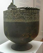 Large black bowl-shaped bucket on a stand. The bucket has incrustation around its top.