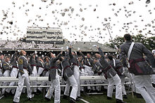 Outdoors men in gray uniforms throwing hats in the air.