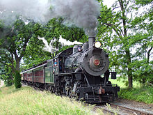 Steam engine pulling passenger cars through a wooded area