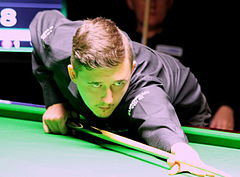 Photograph of Kyren Wilson leaning across the table, holding a cue.
