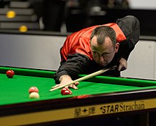 Mark Williams wearing a red waistcoat and black shirt playing snooker at a tournament