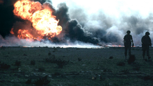 Huge oil fire, with two soldiers in foreground