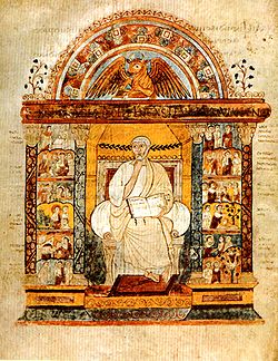 Manuscript illustration of a bearded, white-haired man in white toga, holding a book open, with his other hand at his chin. The man is sitting in a chair in a golden niche, surmounted by a portrait of a winged bull under an arch; at either side of the niche are twelve small group scenes from the Life of Christ (see article on the manuscript for a detailed description).