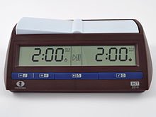 A brown chess clock with blue buttons along the bottom. A digital display shows the time remaining for each side