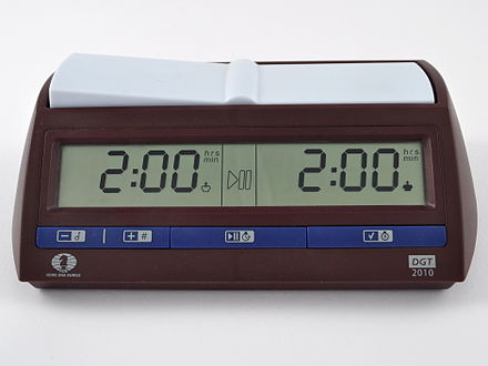 A chess clock with a brown base. A digital display shows the remaining time for each side.