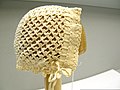 A bonnet, yellowed with age, displayed on a wooden form