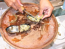Photo of opened oyster in bowl with person using a knife to remove the pearl