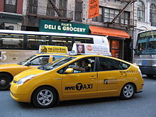 Two yellow taxis on a narrow street lined with shops.