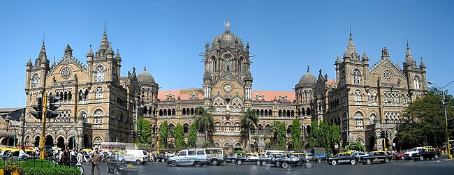 A brown building with clock towers, domes and pyramidal tops. Also a busiest railway station in India.[311] A wide street in front of it