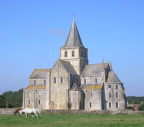A tall church of grey stone with fine details and a crossing tower topped with a slate-covered spire rises out of rural countryside, where two mares are grazing.