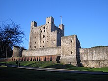 A photograph of a tall stone castle keep; most of the towers are square, but one is circular.