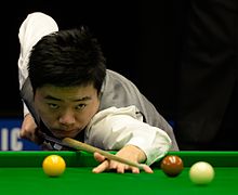 Ding looks down his cue and prepares to take a shot.