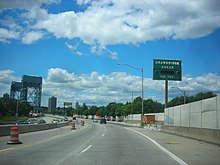 A six lane freeway in an urban area with a vertical lift bridge in the distance. A green sign with flashing lights on the right side of the road reads Drawbridge ahead 700 feet.