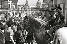 A pair of police officers mounted on horses observe a protest march down a street in San Francisco.