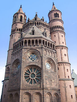 The apsidal end of a tall red stone church framed by circular towers.