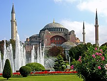 A reddish building topped by a large dome and surrounded by smaller domes and four towers