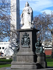 Large figure of a woman wearing a crown and robes, positioned on a tall plinth